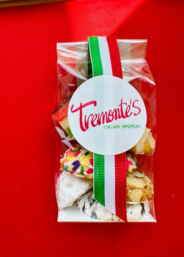 Transparent gift box containing assorted Italian-American pastries, with a logo labeled 'Tremonte's' and a tricolor ribbon of green, white, and red.